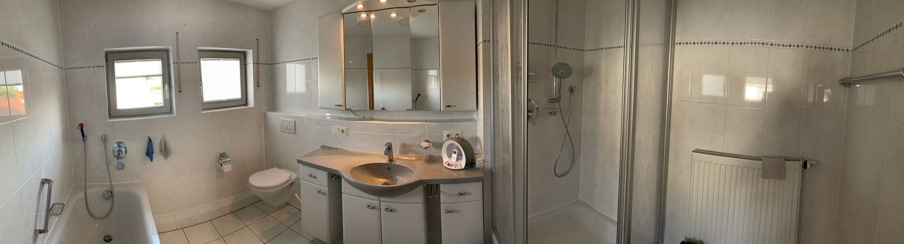Panorama des alten Bades: weiße Fliesen mit blauer Bordüre, Badewanne, Duschkabine mit Kunststofftüren, Spiegelschrank
